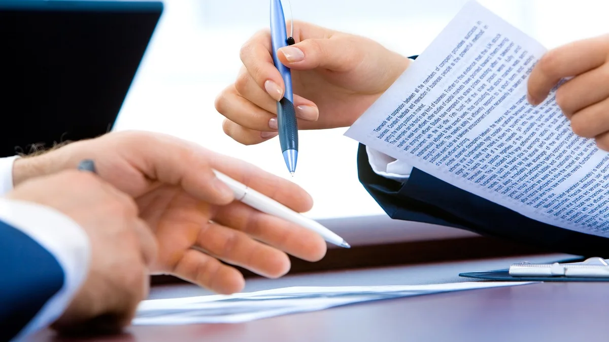 Financial reports and paperwork spread across an office desk with a pen