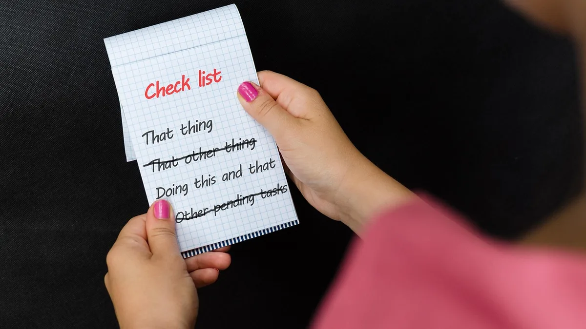 Hands holding a handwritten inventory count checklist on a notepad