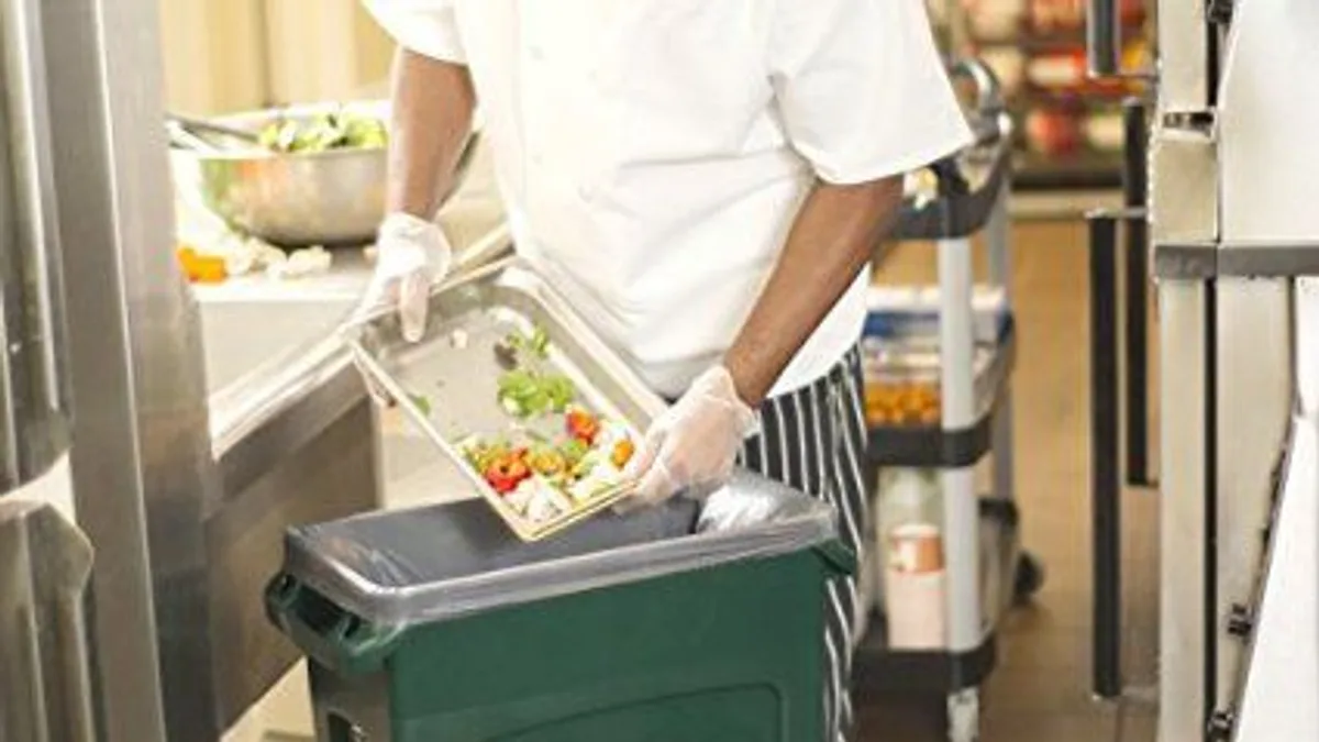 Kitchen worker scraping food scraps into a recycling bin