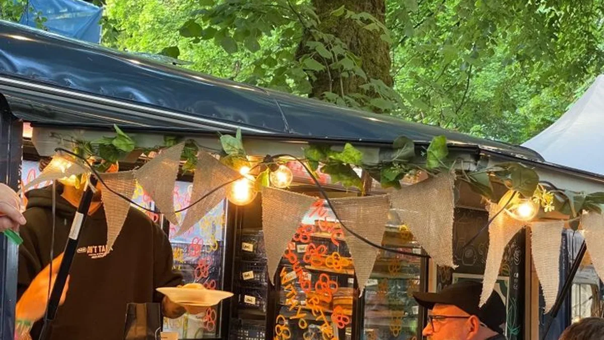 Customers browsing a festively lit outdoor food market stall hung with snacks under string lights