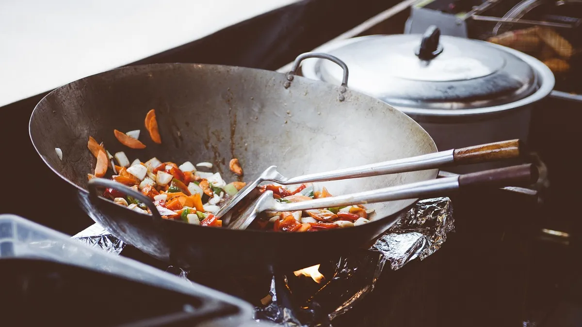 Chef sauteing food over an open flame in a stainless steel pan