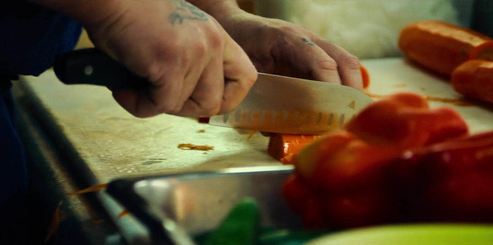 A cook slicing carrots with a chef's knife during prep.