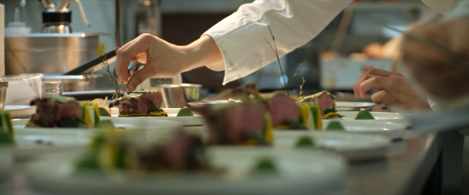 A chef plating several dishes along a busy kitchen line.