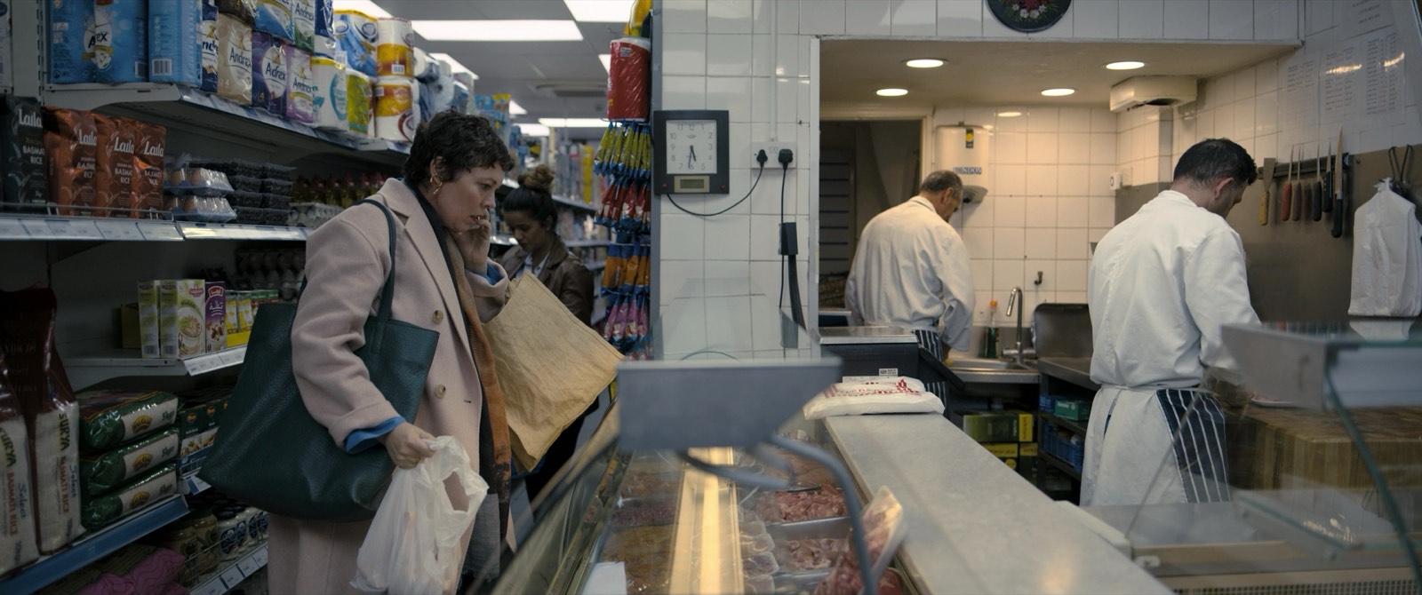 A shopper at a butcher and grocery counter stocked with packaged goods.