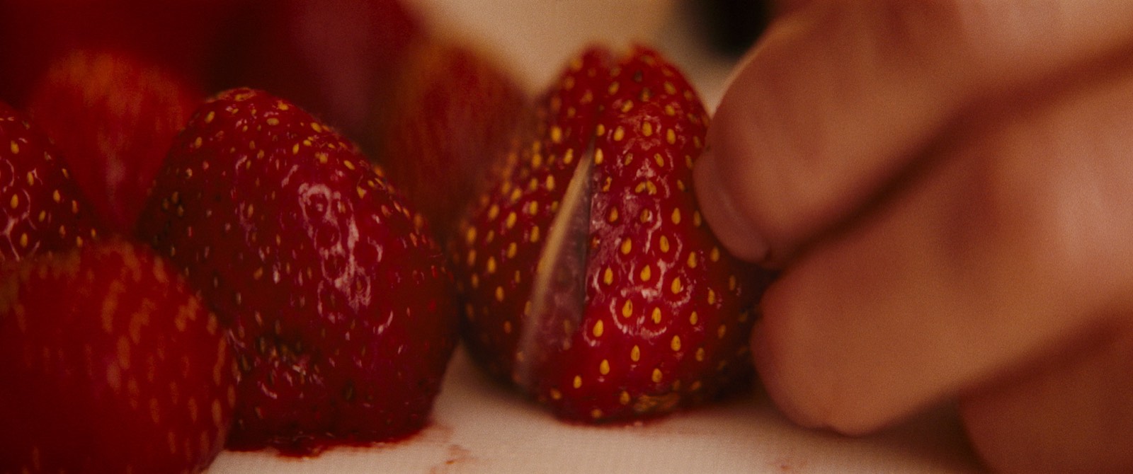 Fresh strawberries being sliced on a cutting board.